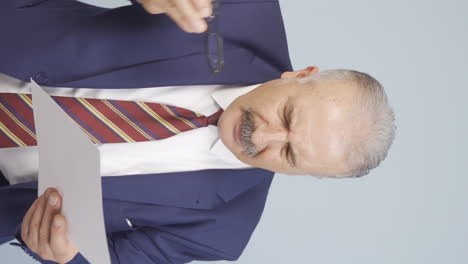 Vertical-video-of-Old-businessman-examines-paperwork-and-gets-upset.